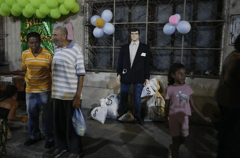 Una figura, etiquetada como corrupto y rodeada de sacos que simulan bolsas de dinero, en una acera antes de que arda durante la celebración de la Quema de Judas, en el vecindario de San Agustín, en Caracas, Venezuela.